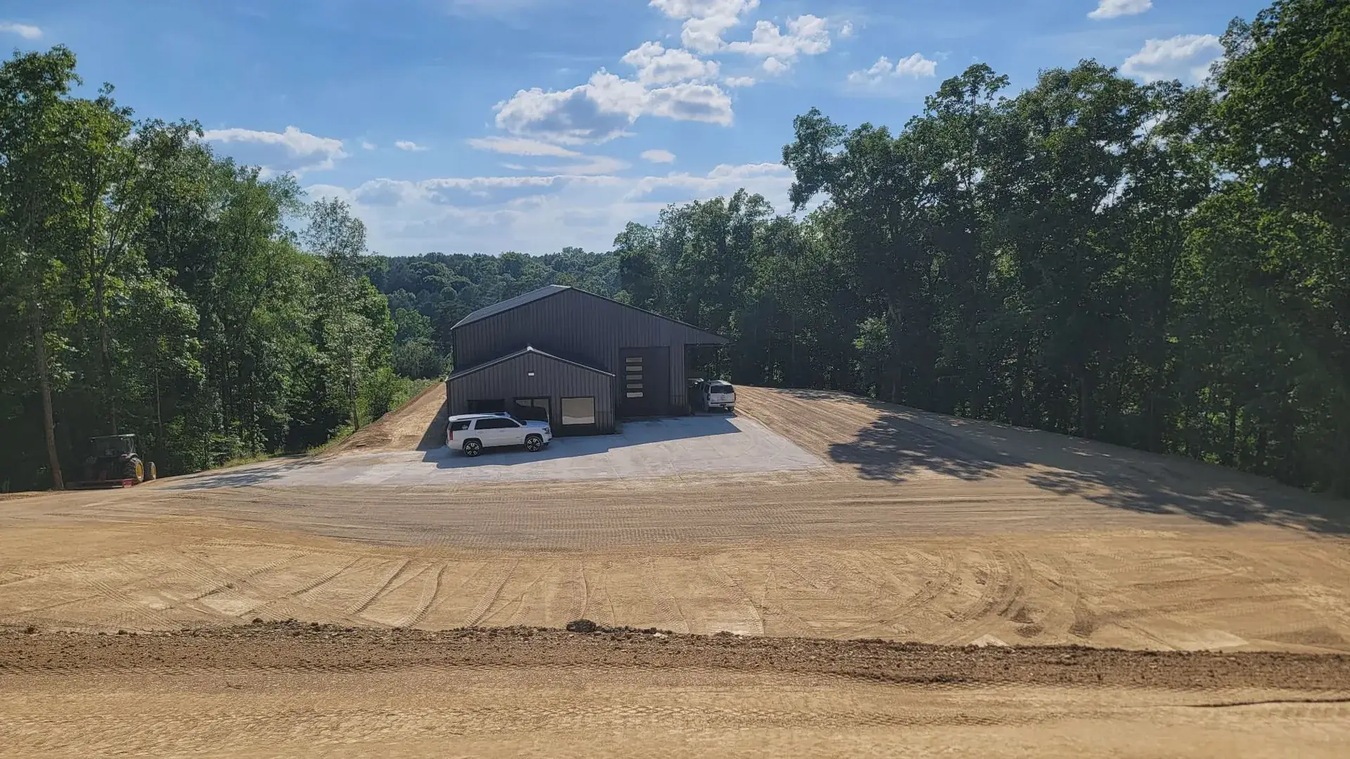 Site graded around a metal building in wooded hills, the kind of ground we work around Jasper