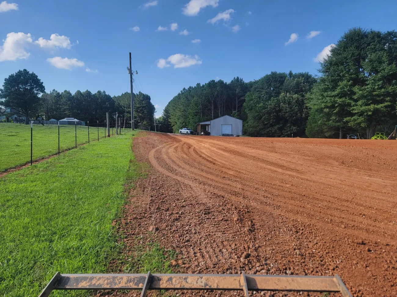 A long strip of red clay rough graded along a fence line