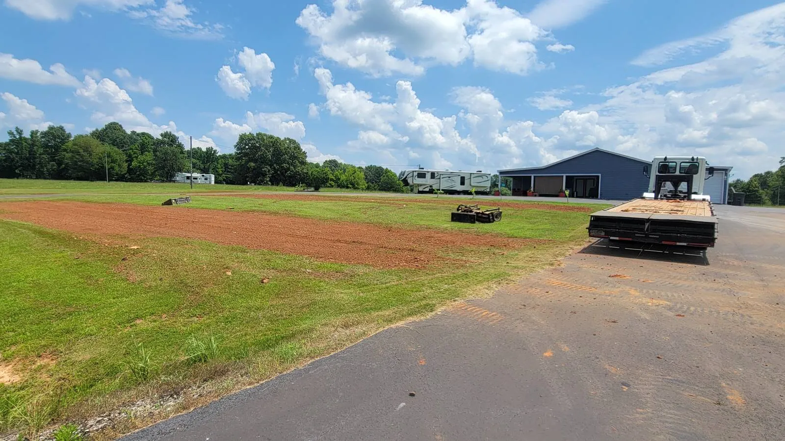 A strip of yard we regraded and raked smooth beside a paved drive, with a metal building behind it